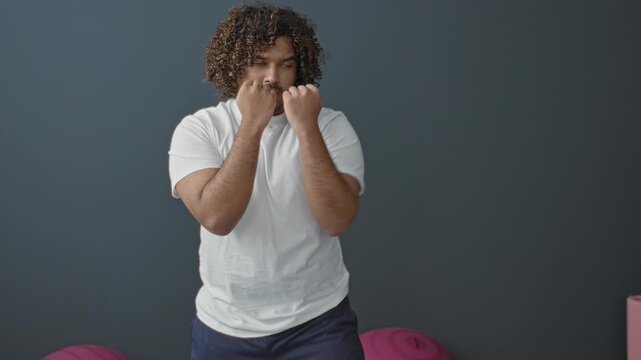 Man in white tshirt with fists guarding face and throwing a jab beside exercise ball in studio; determination training.
