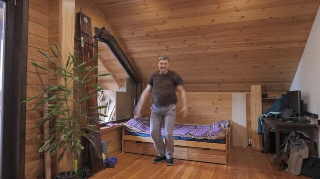 Man performing jumping jacks exercise indoors, active training session in wooden room, dynamic body movement for fitness routine
