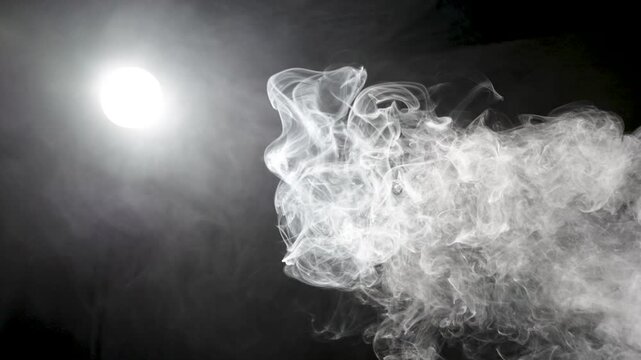 Soft white smoke billows and curls across a dark background, illuminated by a bright glowing light source on the left, creating dramatic contrast and atmospheric depth with copy space