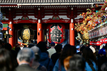 Obraz premium Crowds of visitors walking toward the iconic Kaminarimon gate at Sensoji Temple in Tokyo, featuring the famous red lantern and traditional Japanese architecture.