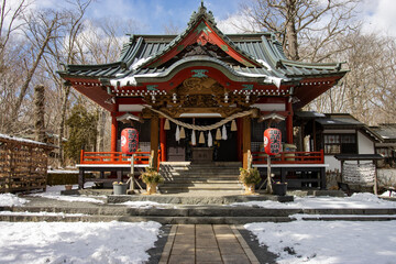 Obraz premium Traditional Japanese Shinto shrine building in winter with snow on the ground, featuring classic architecture and red lanterns.