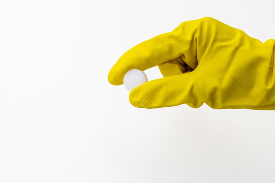 Hand in Yellow Rubber Glove Holding Single White Mothball on White Background