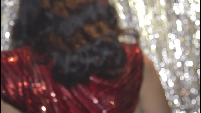 A woman in a shiny dress stands in silhouette against a curtain
