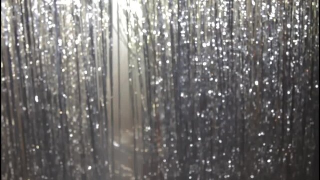 A woman in a shiny dress stands in silhouette against a curtain

