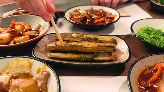 A close-up of a grilled razor clam. A hand picks up a grilled razor clam with a chopstick at an Asian restaurant.