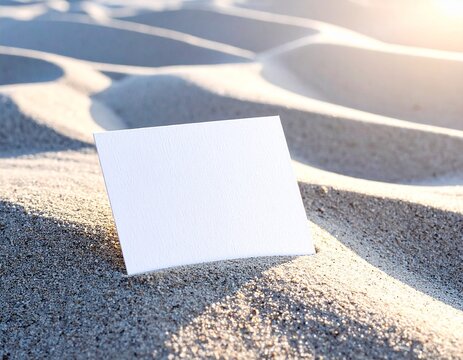 Blank card resting on a sandy beach with soft sunlight creating shadows