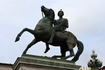 Obraz premium Statua equestre di Polluce in bronzo all'ingresso di Palazzo Reale a Torino, scultura neoclassica dei Dioscuri su piedistallo in marmo con cielo nuvoloso