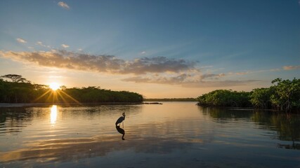 Naklejka premium Serene sunset over a tranquil river with a solitary heron standing amidst lush greenery