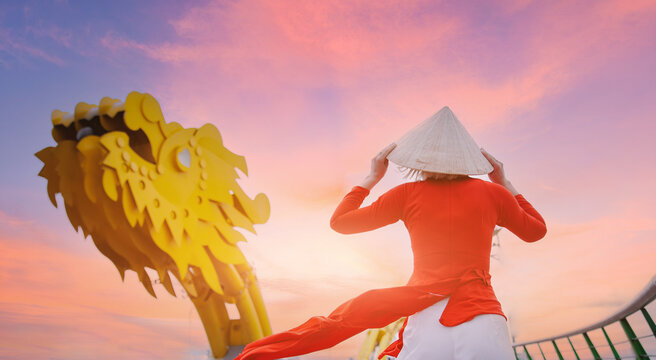 Tourist woman in traditional red dress on background Dragon bridge over Han river in Da Nang, Vietnam