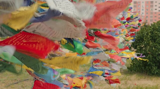 Close-up of colorful Tibetan Buddhist prayer flags with mantras blowing in the wind. Spiritual and peaceful mood. Blurred urban building in the background. Slow motion