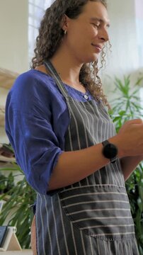 Vertical video: Tapping shop staff reading message on device and laughing at plant shop with apron