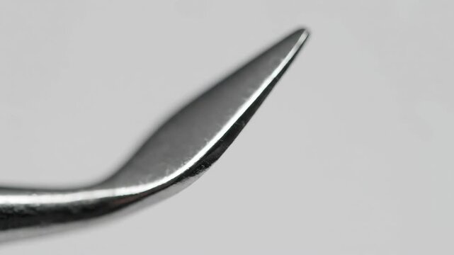 Macro shot of a sharp, curved metallic tool tip on a grey background