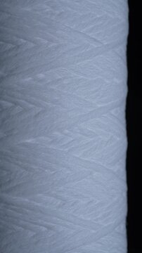 Close up of white polypropylene string wound sediment filter cartridge used for water purification filtration and household plumbing systems, rotates. Texture or background polypropylene water filter