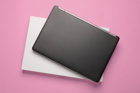 New black modern laptop with white cardboard box on a pink background. Top view