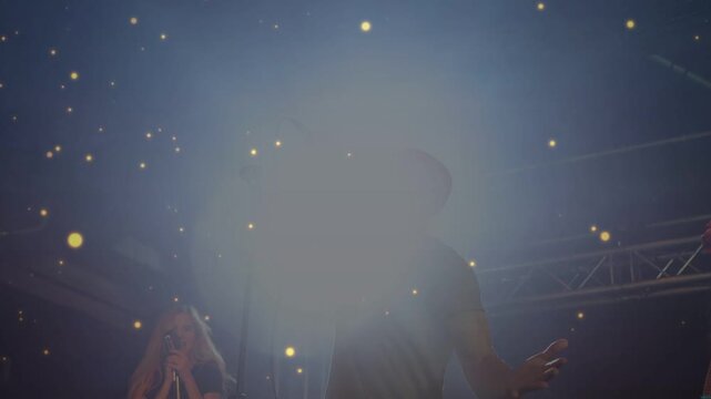 Lead singer singing in music venue, spotlight flare growing and gold particles obscuring trio