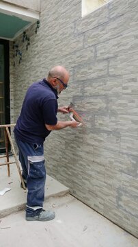 Experienced construction worker grouting stone effect porcelain tiles on an exterior wall