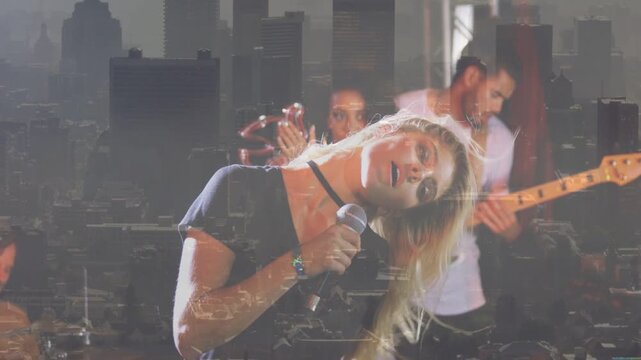 Camera pulling up, lead singer singing into mic, tossing hair, city skyline over band playing music