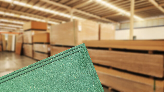 Green particle board sheets (HMR) stacked in a wood warehouse with blurred background. Concept of construction materials, carpentry industry, plywood alternative, and manufacturing supply.
