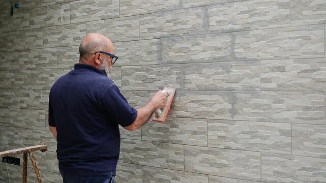 Skilled worker meticulously grouting porcelain stoneware tiles on an exterior wall