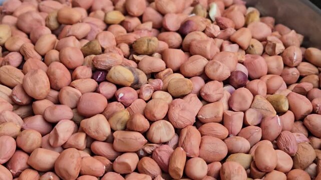Reddish-brown groundnut kernels cascade downward. While most are smooth and healthy, some damaged, appearing shrivelled, discoloured, broken, dried or creating a mix of high and low-quality kernels.