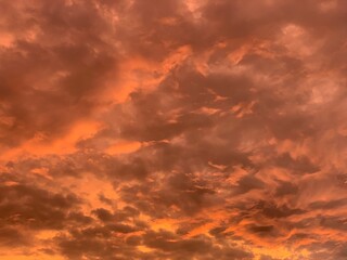 Fototapeta premium Dramatic fiery sky with glowing orange clouds at sunset, soft focus abstract texture, upward angle, rich light and shadow. Evokes intense mood, energy, and warmth. Perfect for backgrounds, nature, wea