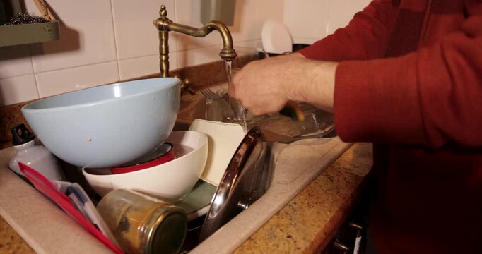 Man washing pile of dirty dishes in kitchen sink