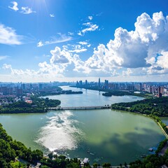 Naklejka premium An aerial view showcases a sprawling cityscape nestled alongside a tranquil lake, framed by lush greenery and a vibrant blue sky dotted with fluffy white clouds.