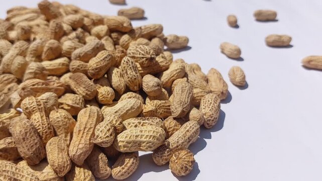 A generous pile of raw organic peanuts in their fibrous shells arranged on a clean white surface for culinary preparation and healthy snacking