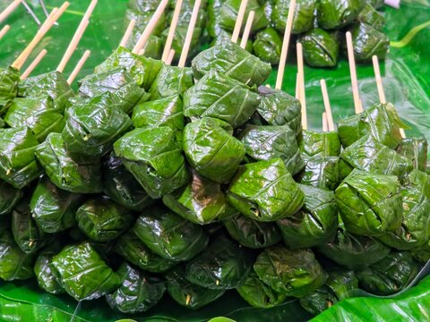 Thai Miang Kham Skewers Wrapped in Wild Betel Leaves on a Green Banana Leaf Base