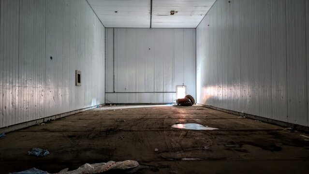 Bare storage unit interior, large square empty room. Light shining through doorway, high ceiling and walls. Deserted logistics warehouse, industrial emptiness. Huge industry recession cargo container