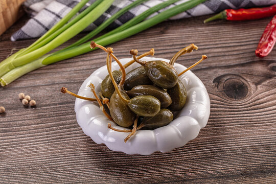 Pickled caper berries in a bowl with fresh ingredients on a rustic wooden table.