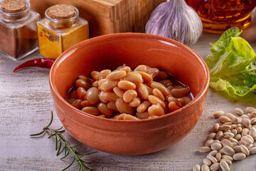 Cooked white beans in a terracotta bowl with fresh vegetables and spices. © Andrei Starostin