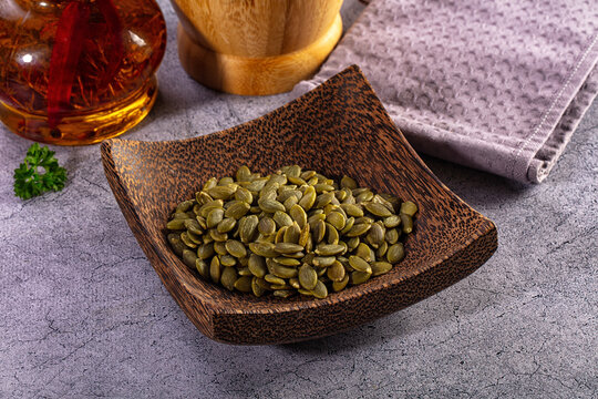 Pumpkin seeds in a dark wooden bowl on a rustic kitchen counter