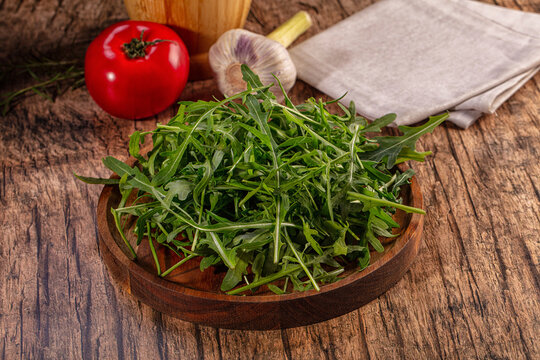 Fresh arugula in a wooden bowl with tomato and garlic on a rustic table