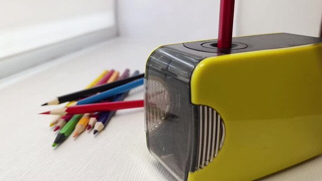 Yellow electric pencil sharpener on a desk with colored pencils