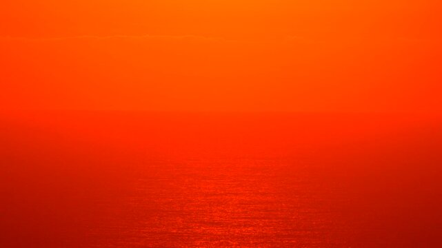 Sunset ocean abstract, fiery orange red background reflecting intense tropical light on the shimmering water surface.