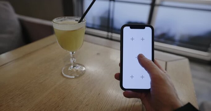 POV of a hand holding a smartphone with tracking markers at a restaurant table, scrolling and tap