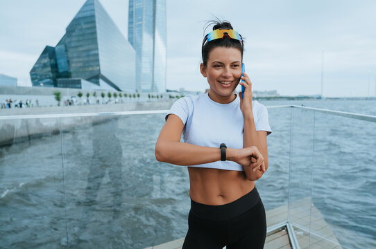 A woman in sporty attire enjoys a phone call by the waterfront, exuding joy and relaxation while embracing the dynamic urban environment around her.