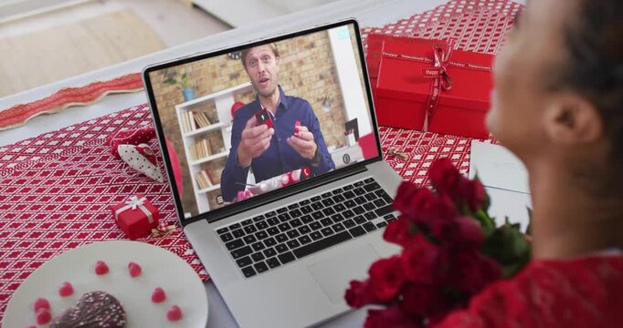 Diverse couple on a valentines date video call man on screen showing ring to woman holding flowers