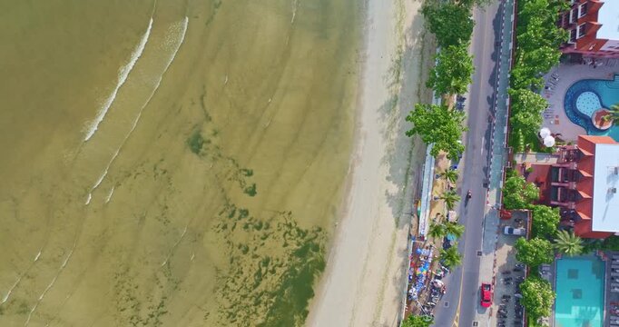 Top view of algae forming along the sandy coast of Patong Beach with machinery working to restore the shoreline. A striking blend of natural textures and industrial activity in a seaside environment
