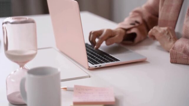 Woman working on laptop, pink computer, office desk with coffee cup and notebook, remote work setup