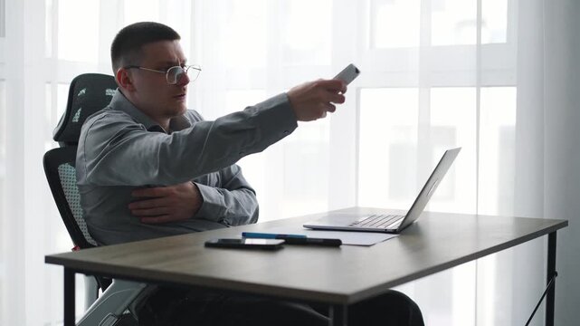 A businessman turns on the air conditioner in his office to warm up.
The office is freezing, and a man is shivering with the air conditioner remote control.