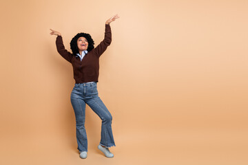 Joyful young businesswoman in casual chic outfit dances with arms raised against beige background