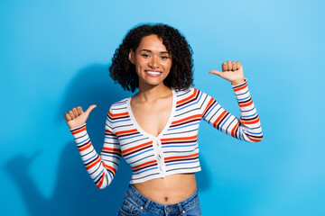 Young chic woman smiles and poses with thumbs up in striped crop cardigan against blue background
