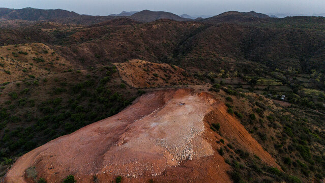 Aerial view of the Aravalli hills near Udaipur, Rajasthan at sunset in spring, showing native vegetation with a cut patch on a hillside for construction.