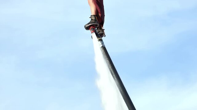 Person flyboarding against blue sky, performing extreme water sport