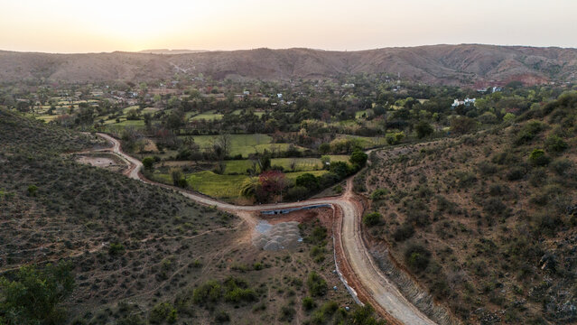 Aerial view of the Aravalli hills near Udaipur, Rajasthan at sunset in spring, showing native vegetation with a cut patch on a hillside for construction.