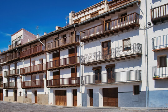 A row of historic, multistory traditional  buildings in a Spanish town, with intricate wooden balconies and white plaster walls, in Morella, Catalonia, Spain
