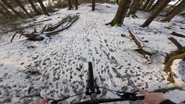 Action camera footage capturing an enduro cross-country mountain biker riding through a Scandinavian forest covered in snow. The scene highlights winter trail conditions, flowing movement, and technic