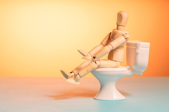 Wooden mannequin sitting on toilet, stomach illness and diarrhea concept